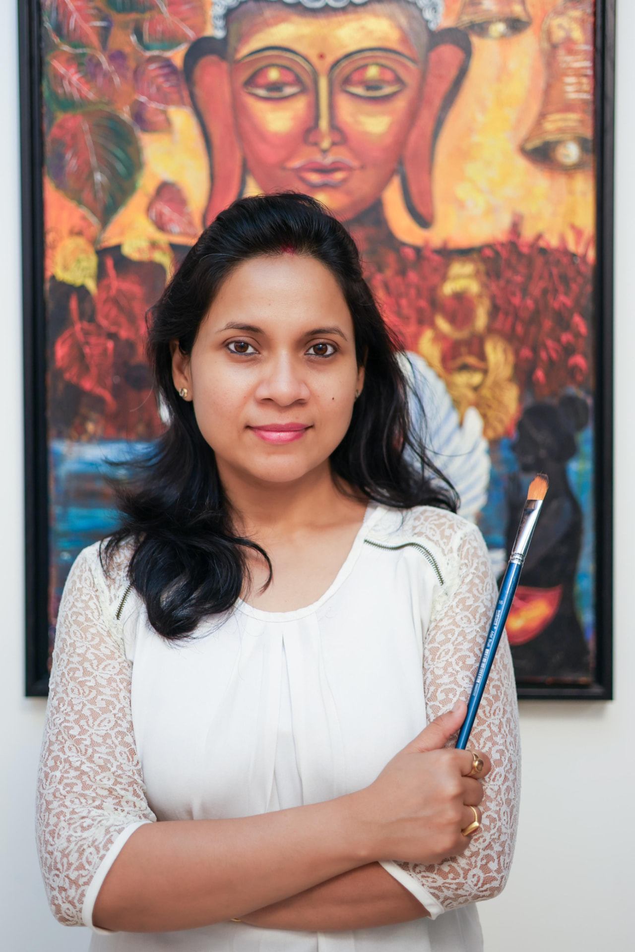 Jayita Dana holding a paintbrush in front of one of her visionary paintings