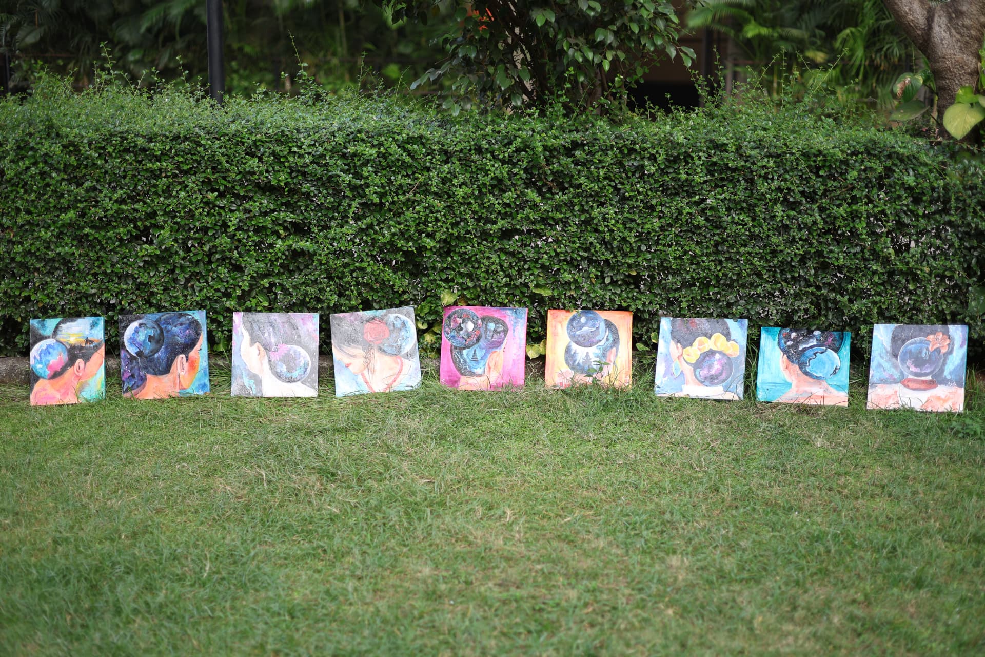 A row of diverse visionary portraits standing on grass against a hedge